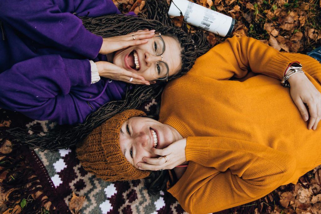 Новини фонду Two friends smiling, enjoying fall colors while lying on autumn leaves outdoors.